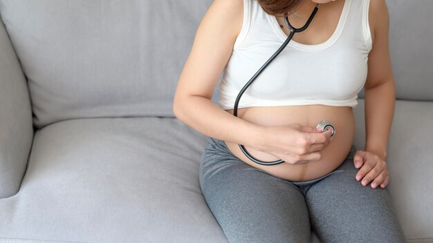 Jeune femme enceinte mettant un stéthoscope sur le ventre concept de soins de santé et de soins de grossesse