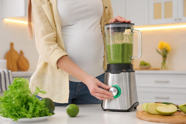 Jeune femme enceinte préparant un smoothie à table dans la cuisine en gros plan