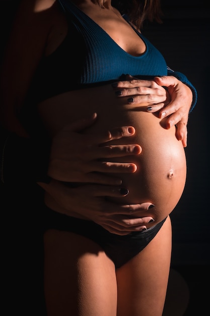 Jeune femme enceinte de race blanche sur le point d'accoucher. Avec les mains de son père et de sa mère sur le ventre du bébé. Dans certaines photos de studio