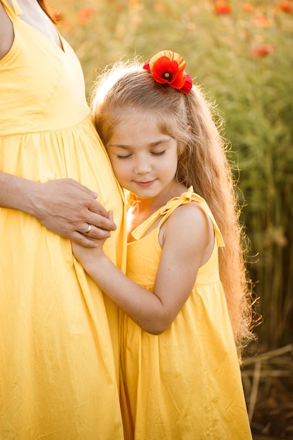 Une jeune femme enceinte avec sa fille en robes jaunes se tient dans un champ de pavot Relations familiales