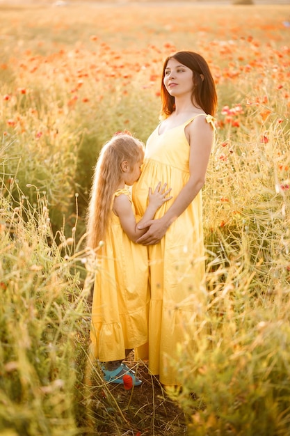 Une jeune femme enceinte avec sa fille en robes jaunes se tient dans un champ de pavot Relations familiales