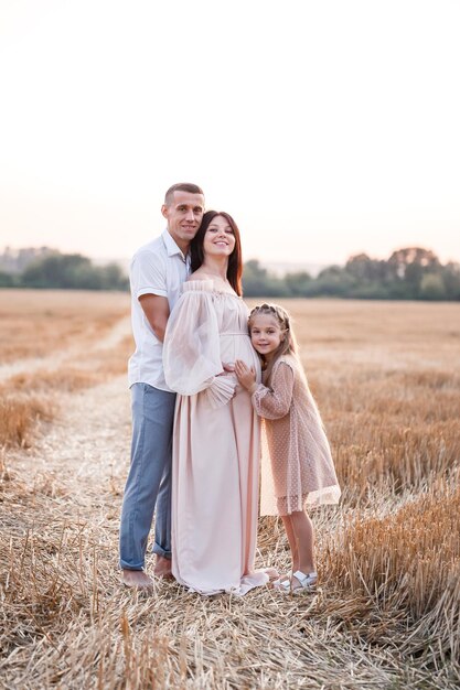 Jeune femme enceinte avec sa fille et son mari famille heureuse étreignant sur un champ doré à la campagne Relations familiales Futurs parents