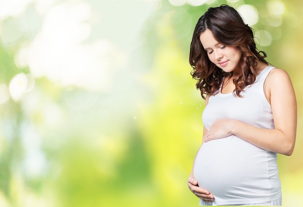 Jeune femme enceinte en vêtements blancs sur fond vert flou