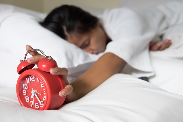 Jeune femme endormie et réveil dans la chambre à la maison