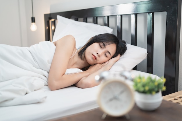 Jeune femme endormie et réveil dans la chambre à la maison