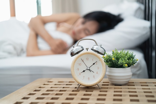 Jeune femme endormie et réveil dans la chambre à la maison