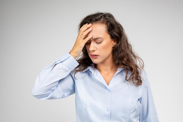 Jeune femme endurant un mal de tête tout en travaillant a souligné l'expression sur un fond neutre