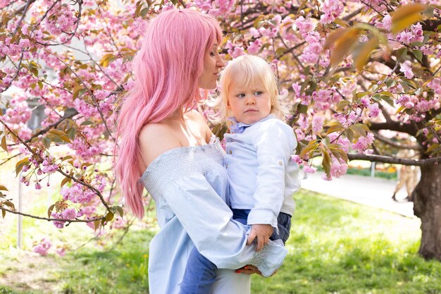 Jeune femme avec un enfant dans ses bras heureux Sakura fleurit au printemps Parc Joie de la maternité et du développement de l'enfant Arbre de fleurs de cerisier à la fin du printemps