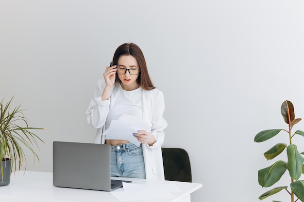 Jeune femme ennuyée vêtue d'une chemise assise sur son lieu de travail