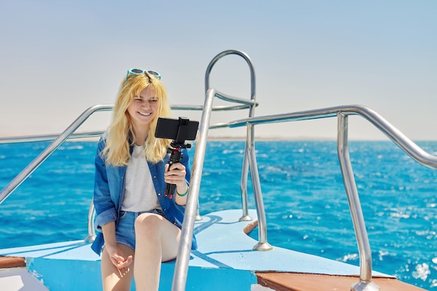 Jeune femme enregistrant un flux sur un smartphone assis à bord d'un yacht en mer