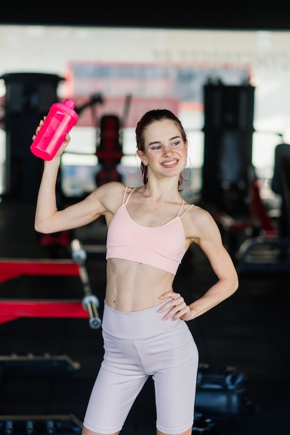 Jeune femme à l'entraîneur de gym tenant une bouteille d'eau