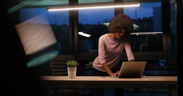 Photo jeune femme entrepreneur afro-américaine indépendante travaillant à l'aide d'un ordinateur portable dans l'espace de coworking de nuit