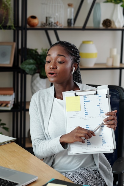 Photo jeune femme entrepreneur pointant sur un document avec un histogramme lors d'une réunion en ligne avec un collègue