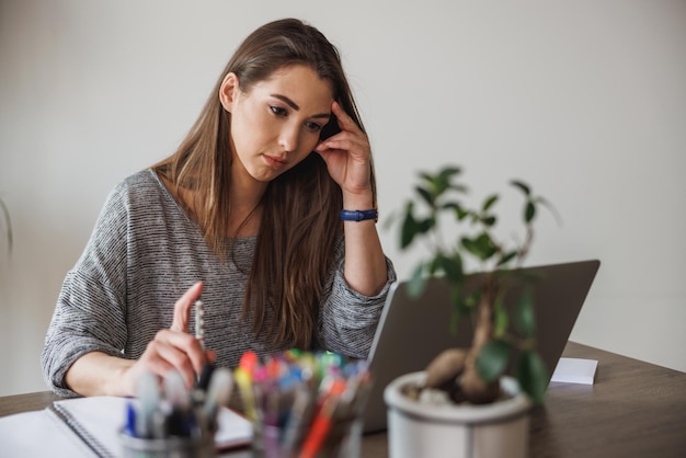 Jeune femme entrepreneur qui a l'air réfléchie tout en travaillant depuis son bureau à domicile.