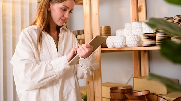 Une jeune femme entrepreneur tenant une tablette vérifiant les produits artisanaux