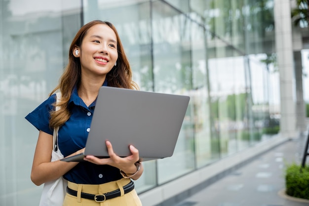 une jeune femme entrepreneur en train de taper sur son ordinateur portable et de parler sur son smartphone avec des écouteurs