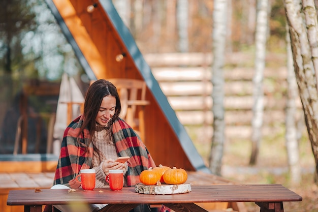 Jeune femme envoyant des SMS sur smartphone et boire du café à l'extérieur