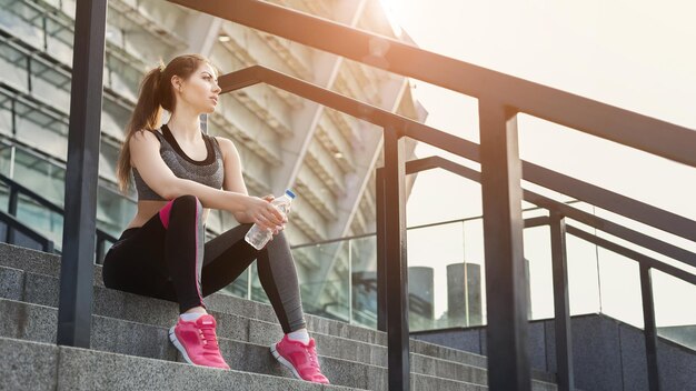 Jeune femme épuisée après s'être entraînée assise dans les escaliers du stade de sport