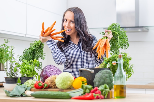 Jeune femme espiègle dans sa cuisine tenant des carottes fraîches dans les deux mains - concept de régime alimentaire et de santé.