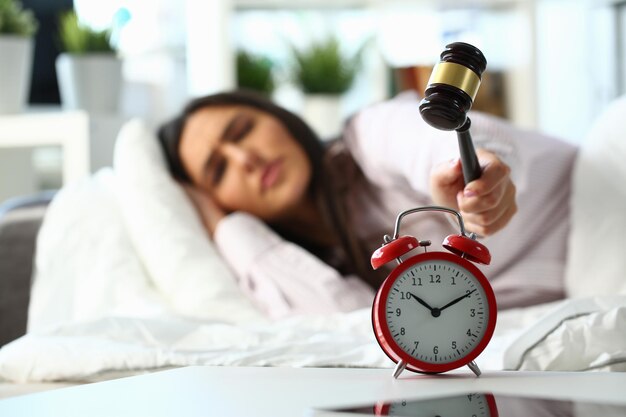 Une jeune femme essaie de briser un réveil avec un maillet en bois et de détruire l'horloge