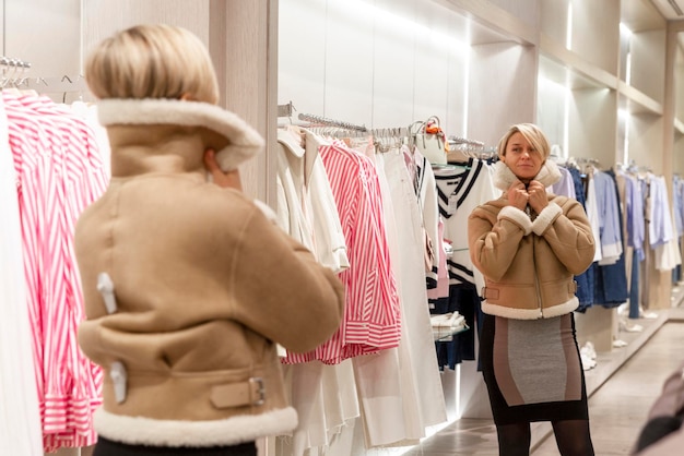 Photo une jeune femme essaie une veste chaude devant un miroir dans un magasin blonde mignonne avec des cheveux courts style et mode