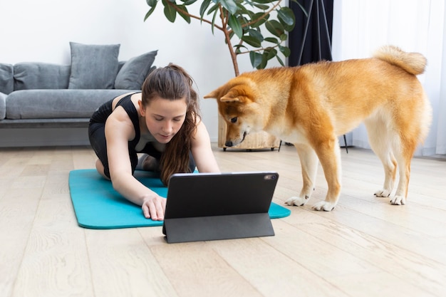 Jeune femme essayant de faire du sport à la maison avec son chien