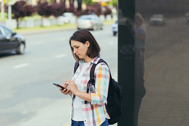 Jeune femme essayant de prendre un taxi à un arrêt de bus à l'aide d'une application à partir d'un téléphone mobile