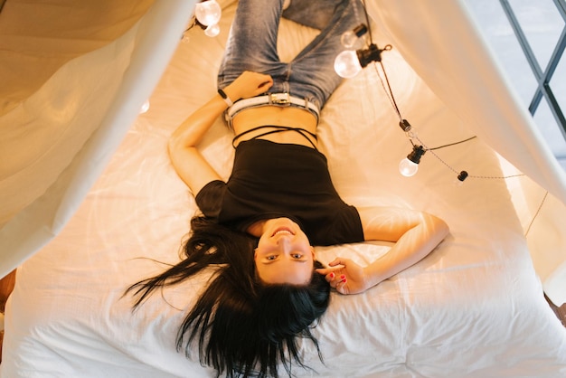 Une jeune femme est allongée dans un lit à quatre volets avec des ampoules lumineuses.