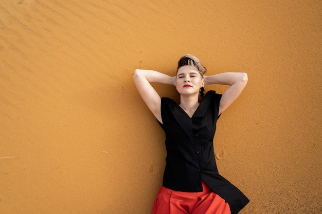 Photo la jeune femme est allongée sur le sable les yeux fermés