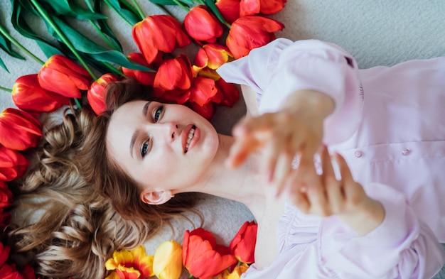 Une jeune femme est allongée sur le sol parmi les tulipes rouges Le concept du 8 mars Saint Valentin Printemps portrait d'une femme