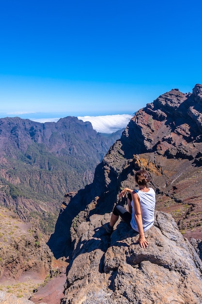 Photo une jeune femme est assise au repos et en regardant la vue sur le parc national de roque de los muchachos au sommet de la caldera de taburiente, la palma, îles canaries. espagne