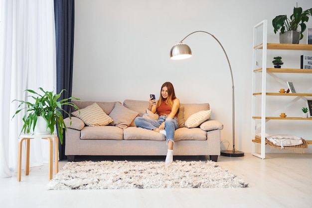 Une jeune femme est assise sur le canapé dans la chambre domestique.