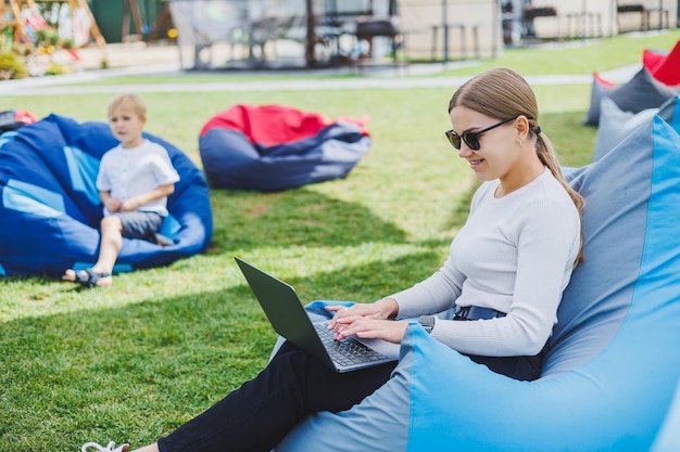 Une jeune femme est assise sur une chaise douce dans le parc et travaille sur un ordinateur portable