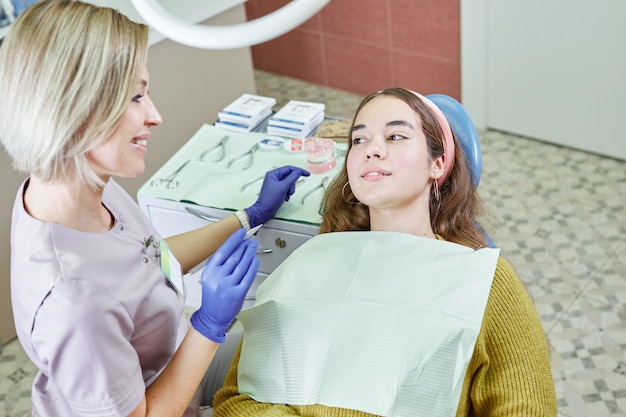 Une jeune femme est assise dans un fauteuil dentaire dans le bureau de la clinique dentaire. Médecin et patiente.