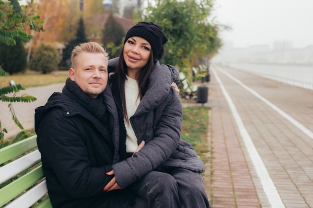 Une jeune femme est assise sur les genoux de son homme sur la promenade dans le froid de l'automne