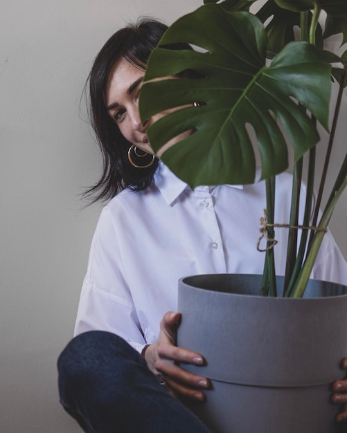 Une jeune femme est assise avec un grand pot de fleur avec monstera