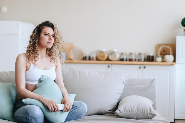 Une jeune femme est assise en haut de sport sur un canapé moelleux dans une maison confortable avec un intérieur clair