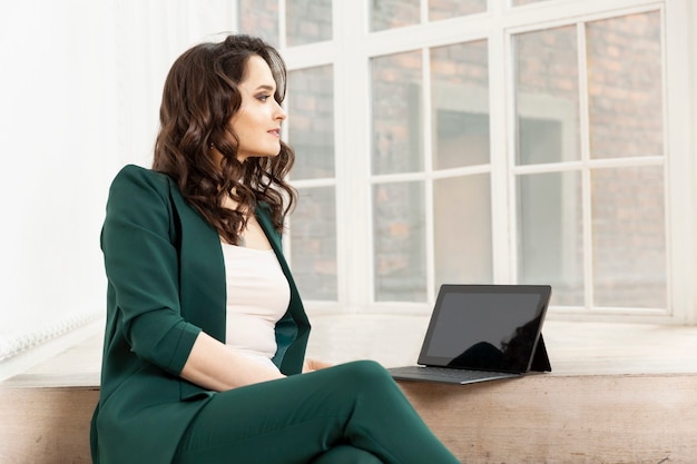 Une jeune femme est assise avec un ordinateur portable. Brune en costume vert. Commerce en ligne et réseaux sociaux.