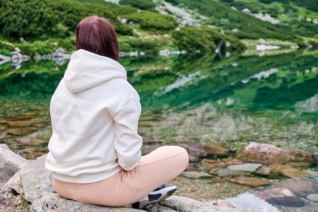 Jeune femme est assise sur la rive du lac avec de l'eau claire et transparente et profitez d'une vue avec espace copie. Détente et méditation sur le concept de la nature.