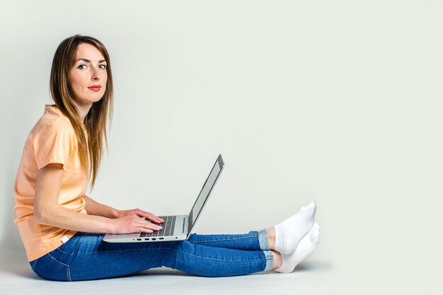 Jeune femme est assise sur le sol et travaille sur un ordinateur portable sur un espace lumineux. Bannière. Concept indépendant.