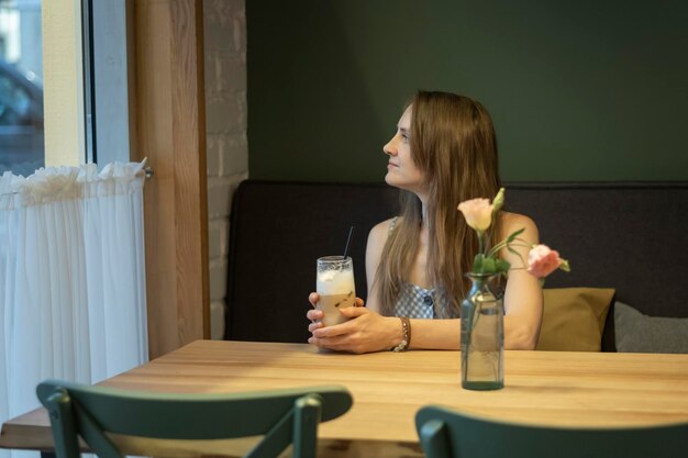 Une jeune femme est assise à table dans un café et regarde par la fenêtre Une jeune femme réfléchie est assise dans un café confortable et confortable