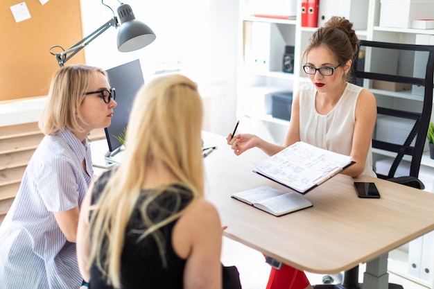 Une jeune femme est assise à une table dans son bureau et parle à deux partenaires.