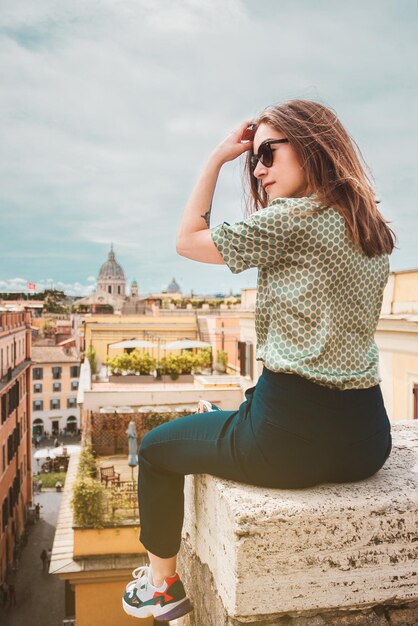 Photo une jeune femme est assise sur un toit avec une vue panoramique sur rome, en italie.