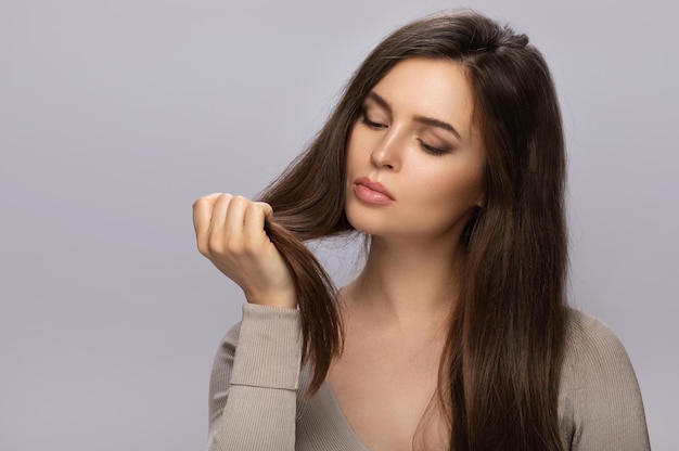 La jeune femme est contrariée par le mauvais état de ses cheveux sur fond gris