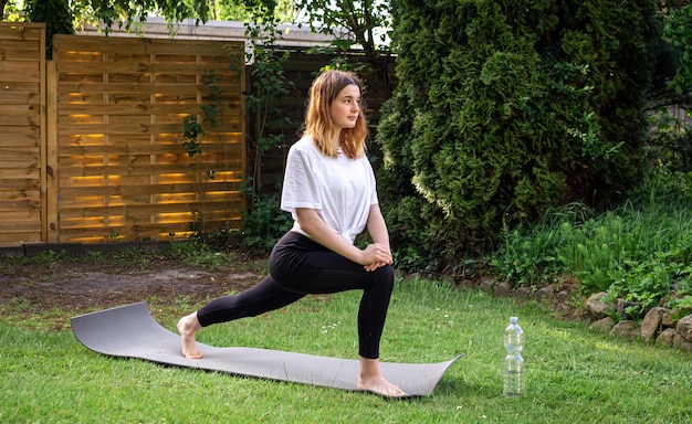 Une jeune femme est engagée dans le fitness dans la nature sur un tapis