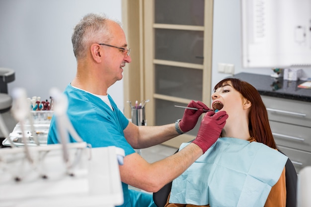 Une jeune femme est venue voir le dentiste, assise dans le fauteuil dentaire avec la bouche ouverte. Senior homme souriant dentiste vérifiant ses dents. Concept de patient et dentiste heureux.