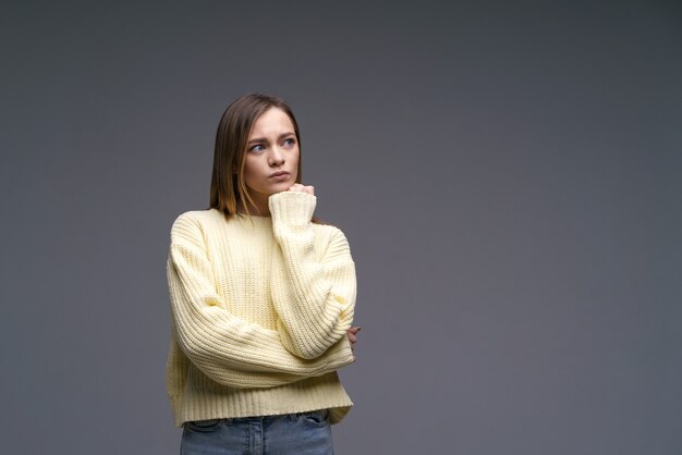 Une jeune femme d'ethnie caucasienne très énervée dans un pull jaune sur fond gris tient sa c...