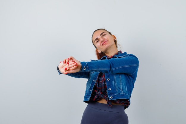 Jeune femme étirant les mains vers l'avant en chemise à carreaux, veste en jean et à la recherche de sommeil.