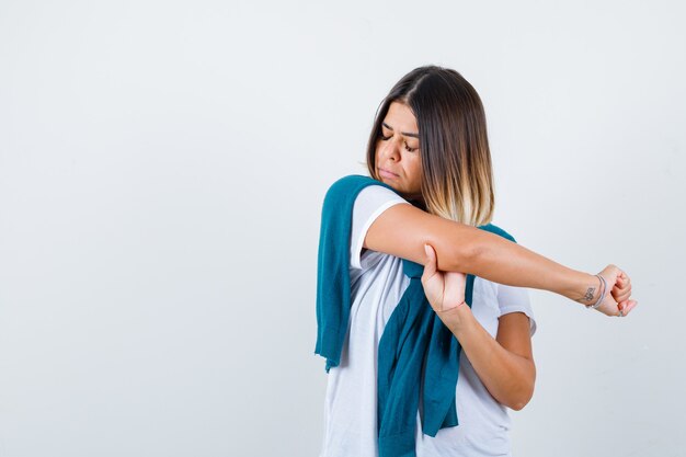 Jeune femme étirant son bras en t-shirt blanc et l'air fatigué, vue de face.