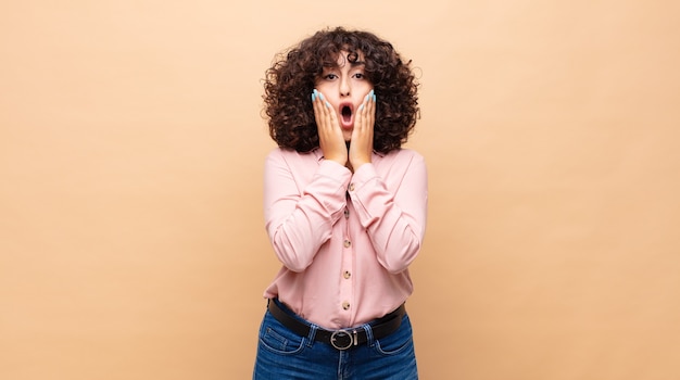 jeune femme étonnée aux cheveux bouclés et une chemise rose